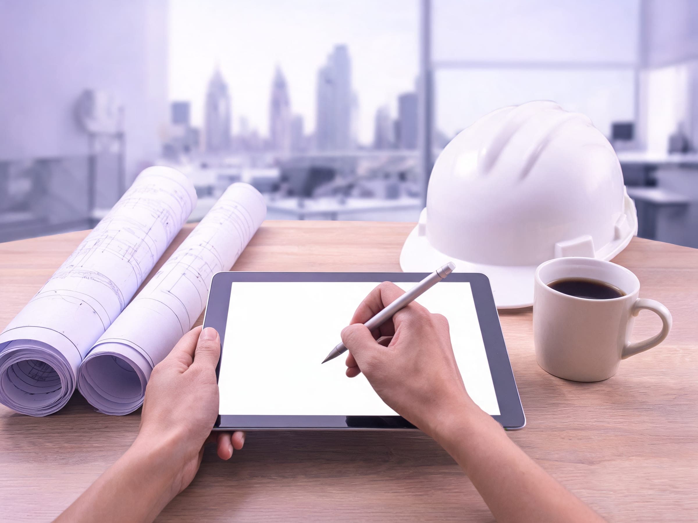 Hands signing on a tablet beside rolled-up plans, a hard hat and a coffee, in a Dubai office